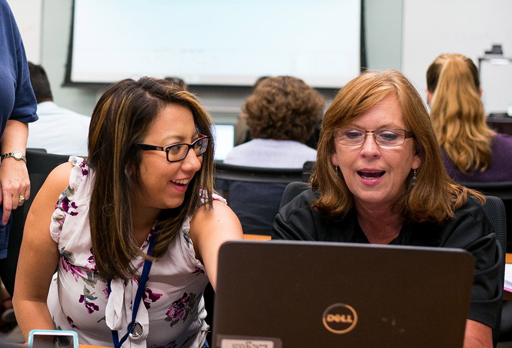 A teacher helps another teacher at a computer